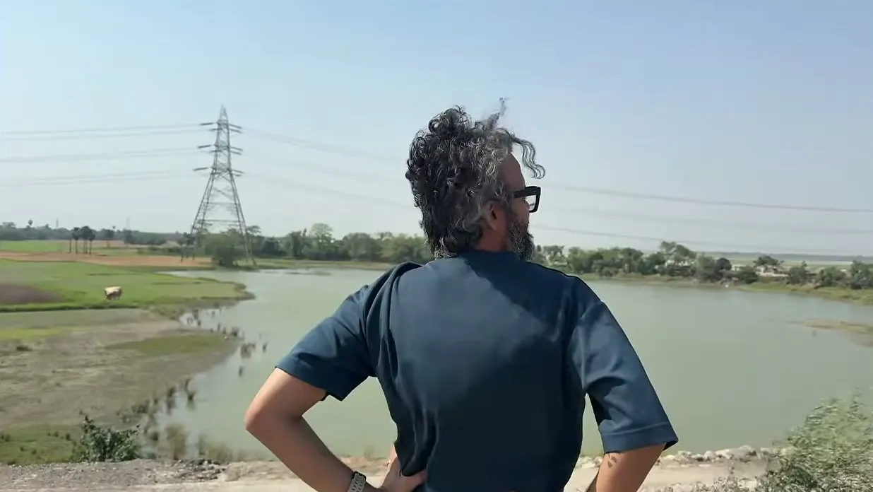 Meghnad looking out over a river, with power lines on the far bank